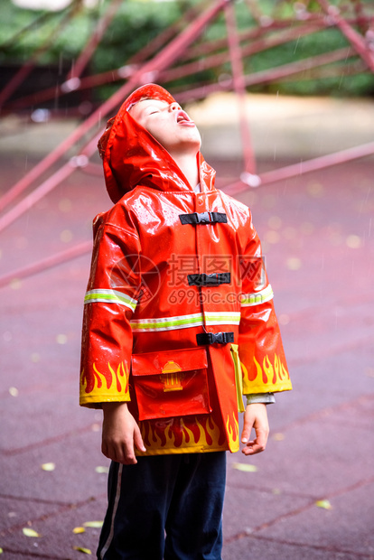 穿着红色消防员雨衣的有趣孩子在雨天公园玩耍图片