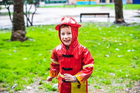 穿着红色雨衣的有趣孩子消防员在雨天公园玩耍图片