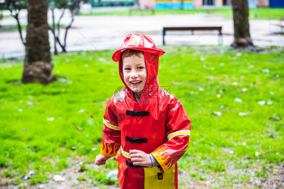 穿着红色雨衣的有趣孩子消防员在雨天公园玩耍图片