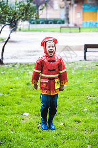 穿着红色雨衣的有趣孩子消防员在雨天公园玩耍图片