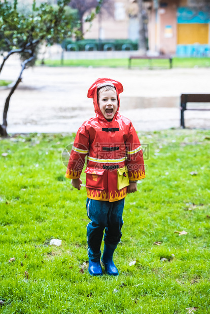 穿着红色雨衣的有趣孩子消防员在雨天公园玩耍图片