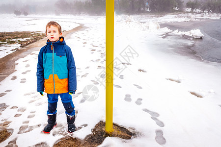 一个男孩站在离散器旁边坚持在一个雪天图片