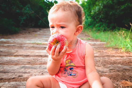 一个年幼的婴儿坐在森林里以苍白的方式喂食咬苹果图片