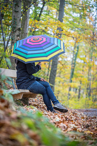 穿蓝大衣和雨伞的年轻女孩正在秋季森林散步图片