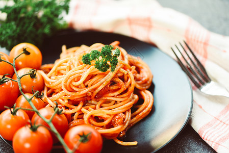 意大利面食在餐厅的黑盘上配有番茄和面食图片