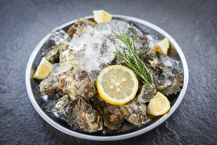盘上黑底的新鲜牡蛎海鸡壳配有草药香料柠檬迷糖餐桌和冰健康海菜图片