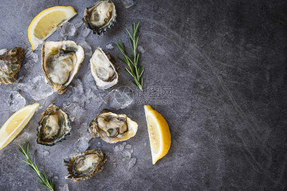 海鲜黑盘底的海鲜露天牡蛎贝壳配有草药香料柠檬迷迭餐桌和冰健康海食品生牡蛎晚餐在厅美食中图片