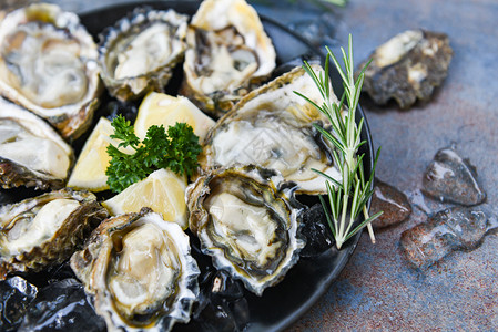 黑板背景的新鲜牡蛎海露天牡蛎贝壳配有草药香料柠檬迷迭面糖在餐厅美食中桌和冰上健康的海鲜生牡蛎食品图片