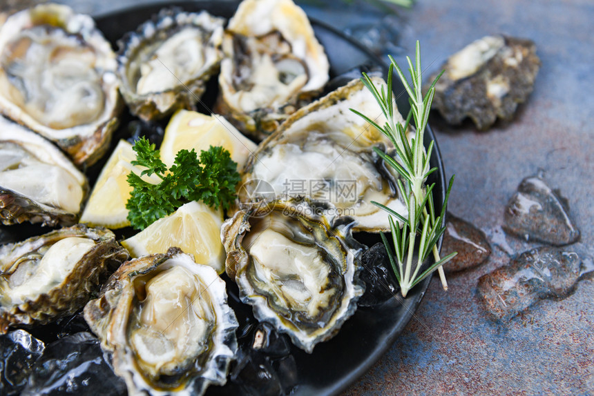 黑板背景的新鲜牡蛎海露天牡蛎贝壳配有草药香料柠檬迷迭面糖在餐厅美食中桌和冰上健康的海鲜生牡蛎食品图片