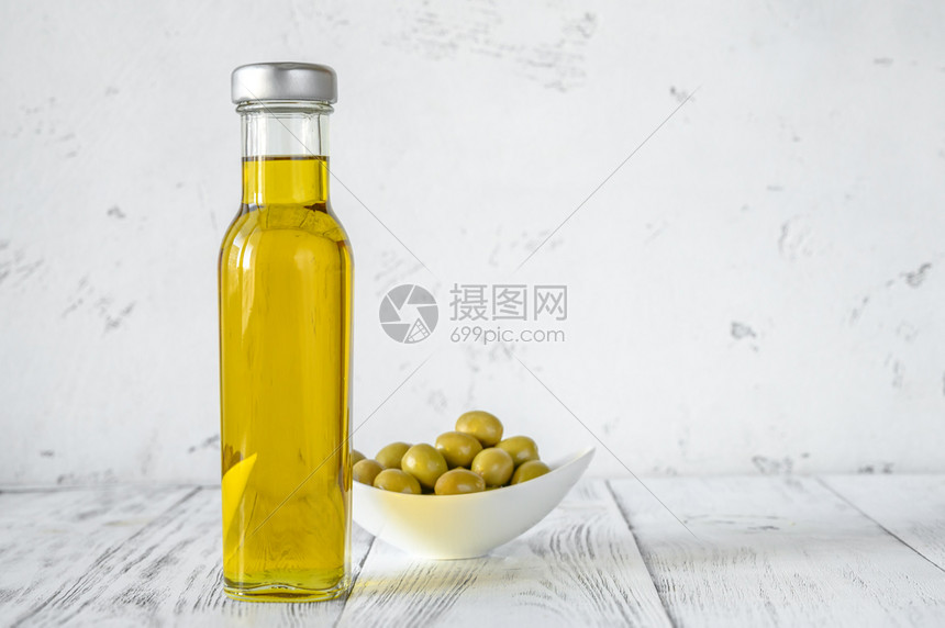 瓶装含绿橄榄的油木制背景图片