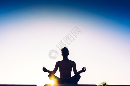 一个人用瑜伽莲花和后面的太阳做姿势休眠孤立在蓝天上图片
