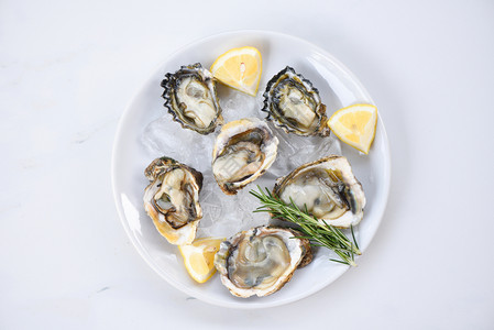 白板底面的新鲜牡蛎海露天牡蛎贝壳配有草药香料柠檬迷迭剂在餐桌上供应厅美食中供应冰上健康海鲜食品图片