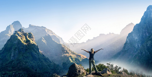 快乐的女子与举起手站在一了解山区和范围日落的背景图片