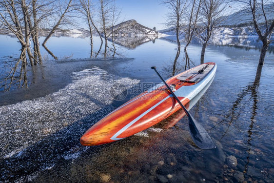在一个部分冰冻湖科罗拉多北部的马牙储藏冬季滑板健身和培训概念上用桨和安全套带挂在一个部分冷冻的湖上北科罗拉多州的马牙储藏健身和培图片