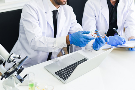 科学家研究小组正在实验室中工作男医生研究者正在实验室生物化学遗传实验室中用显微镜和笔记本电脑进行血液检验结果概念的调查图片