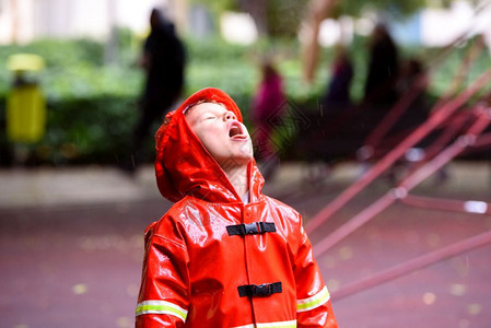 穿着红色雨衣的有趣孩子消防员在雨天公园玩耍图片