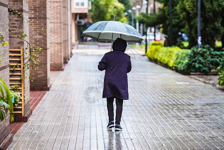 一名成年男子在雨天带着一把黑色雨伞走在城市的街道上图片