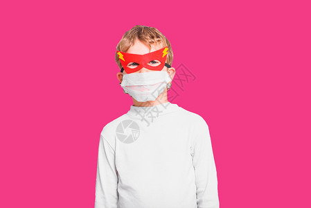 一个带着超级英雄面具保护自己免受感染的男孩被粉红色背景隔离图片