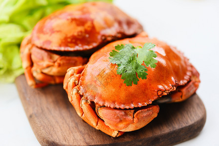 新鲜海石蟹螃煮蒸汽或用白底木板上的沙拉蔬菜煮图片