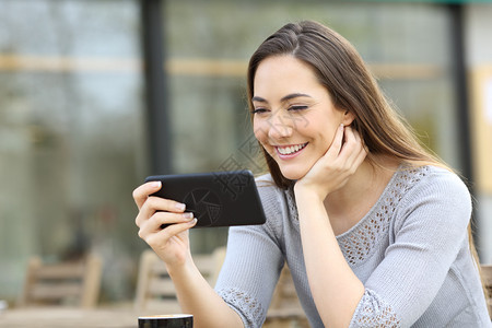 在咖啡店露台观看智能电话在线视频的快乐妇女图片