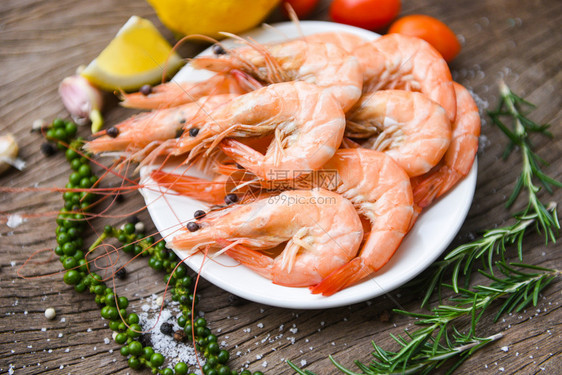 白盘上新鲜虾配有饲料草药和香烹饪的海鲜虾配有木制餐桌背景的虾图片