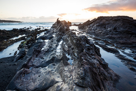 南萨罗特州加那利岛上空的大西洋日落时海浪冲向岸岩石图片