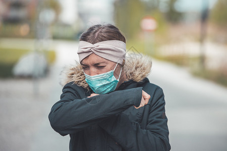 穿面罩的在户外打喷嚏年轻女子科罗纳和流感季节图片