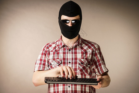 疯狂的黑客男人穿着色的balaclava拿着电脑键盘网上的仇恨言论图片