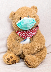 新冠病毒概念:带医疗面具的泰迪熊握住红外前额温度计(高)图片
