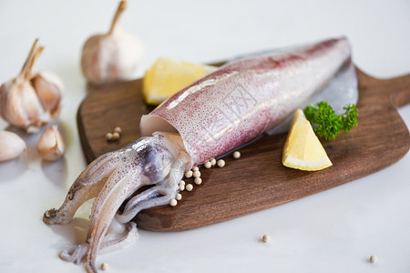 切菜板上的生鱿鱼和白板背景的沙拉香料加柠檬大蒜新鲜乌贼章鱼或餐饮海鲜市场煮熟食品的鱼图片