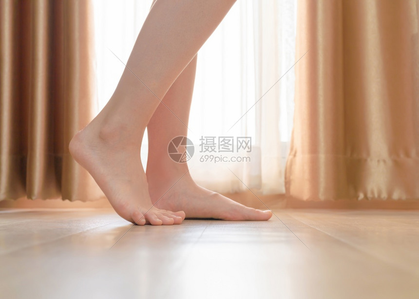妇女脚踩着窗帘的木地板赤脚女孩站在现代住宅或有木地板的公寓室内