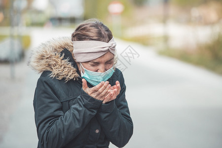 穿面罩的在户外打喷嚏年轻女子科罗纳和流感季节图片