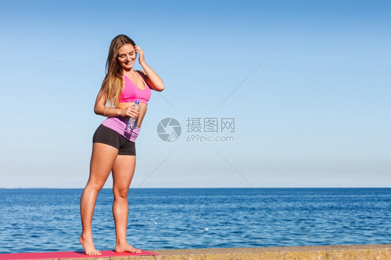 穿运动服的妇女休息用塑料瓶水补充饮用在海边户外运动锻炼后休息图片