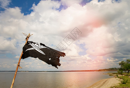 黑褐色海盗旗JollyRoger身穿的殉难者在河流和阴云的天空背景下挥舞棍子黑色海盗旗图片
