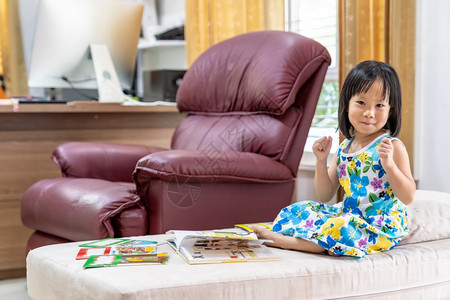快乐的亚洲女孩肖像在家里客厅阅读互动书籍作为家庭教育而城市则因为世界各地的共食19次流行病而被封锁家舍林的概念图片
