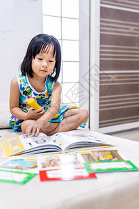 亚洲女童在家里客厅阅读互动式书作为家庭学校教育而城市则因为全世界可食19种流行病而被封锁家舍林为学龄前概念做准备背景图片
