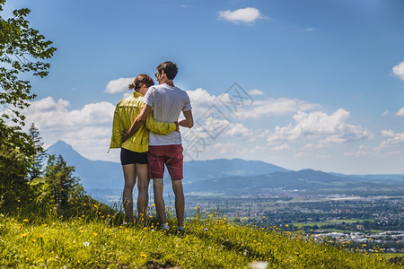 夫妇徒步旅行站在草地上享受远城风景图片