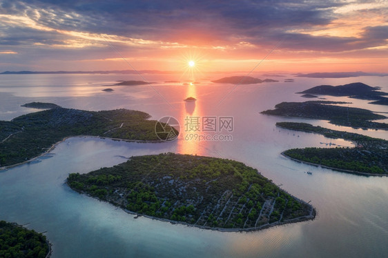 克罗地亚夏季日落时得里海美丽的小岛空中景象蓝水山上的绿树多彩天空云和橙色的太阳图片