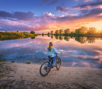 日落时在河岸边上骑自行车的女子图片