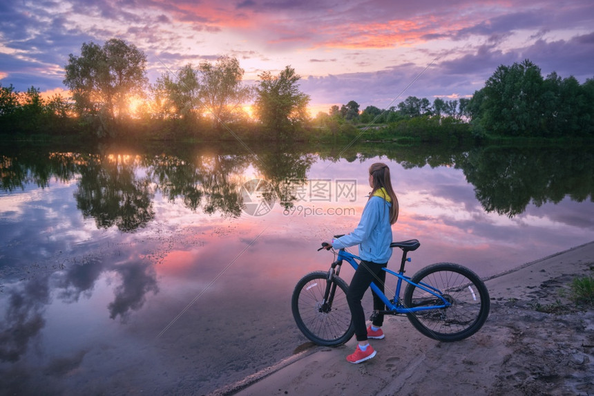 日落时在河岸边上骑自行车的女子图片