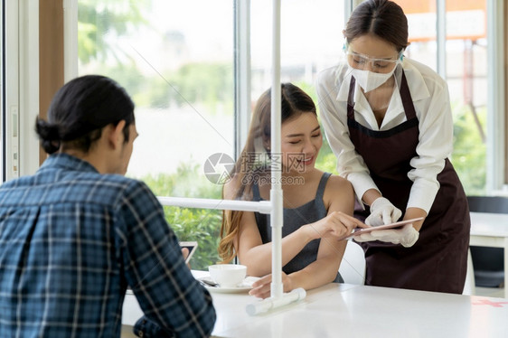 亚洲女服务员用平板电脑显示餐厅子菜单并向顾客推荐新的普通技术和生活方式食品餐饮概念图片