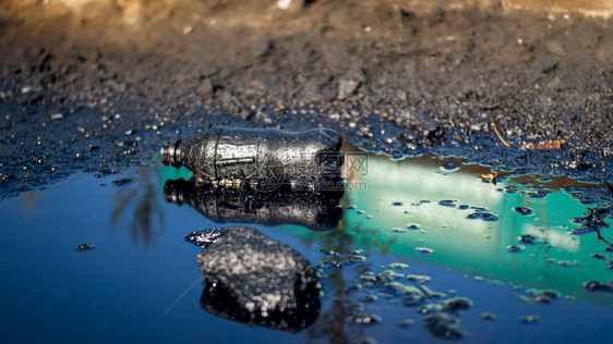 被石油和有毒废物污染的泥地上塑料瓶的胶片沾染着石油和有毒废物污染的泥地上塑料瓶的胶片对环境和生态危害的概念图片