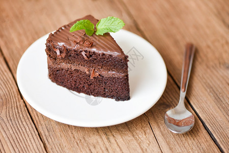 木制餐桌白盘上的蛋糕切片加了巧克力和薄荷叶图片