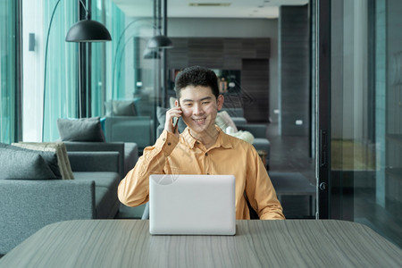 快乐笑的年轻亚洲商人肖像使用笔记本电脑工作在家会议室用智能手机谈论技术设备概念图片