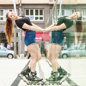 快乐的年轻女子穿着滑冰在镜子墙旁边的小镇上骑马图片