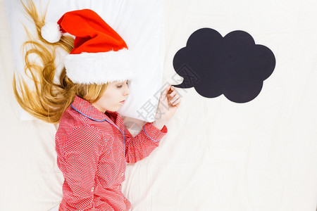 睡着衣和圣诞老人的帽子躺在床上梦想着庆祝节日图片
