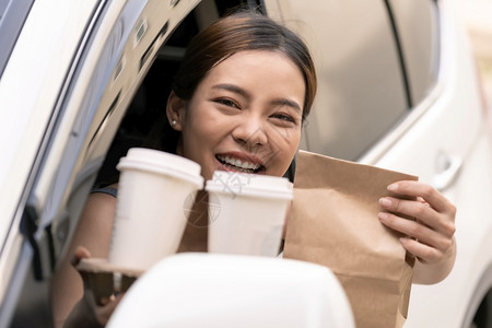 汽车中拿着一次性袋子和咖啡的女人图片