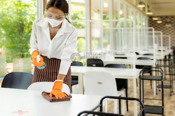 有吸引力的亚洲女服务员脸部戴面罩在欢迎顾客之前用酒精和湿擦洗桌罩新的普通卫生餐厅概念图片