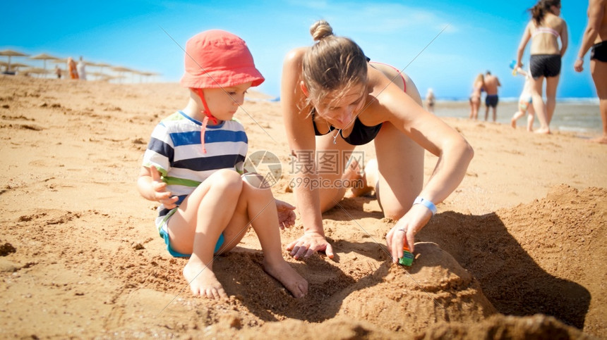 照片来自3岁的幼儿男孩与年轻母亲一起在海滨建造沙堡家庭在暑假期间放松和玩乐照片来自3岁的幼儿男孩与年轻母亲一起在海滨建造沙堡家庭图片