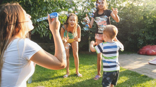 喜悦快乐的年轻家庭在后院花园吹香皂泡喜悦的年轻家庭吹风和香皂泡在家庭后院花园吹香皂泡的有趣肖像图片